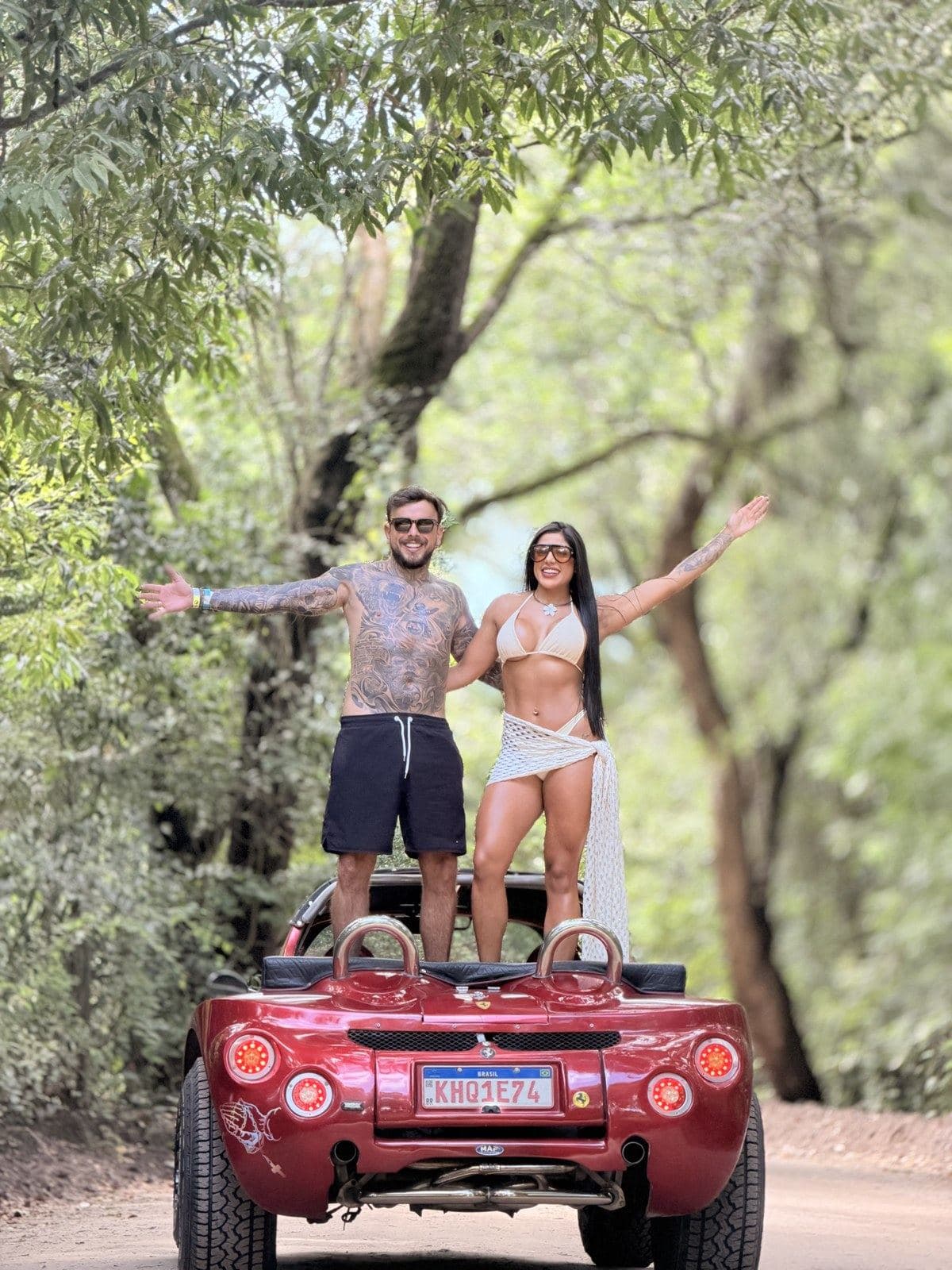 Casal em pé no buggy vermelho em trilha arborizada